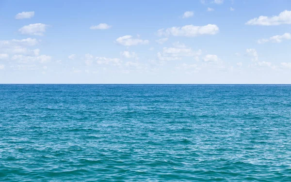 Mavi gökyüzü ve beyaz bulutlarla berrak deniz ufku.