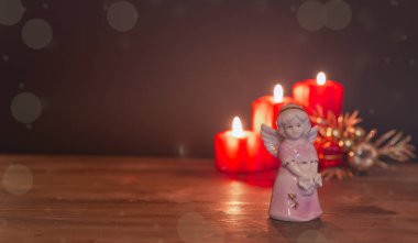 Ahşap bir masanın üstündeki cam melek ve yanan kırmızı mumlar. Boşluğu kopyala