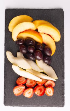 Taze meyve. Çilek, armut, üzüm ve şeftali, taş bir levhada kesilmiş.