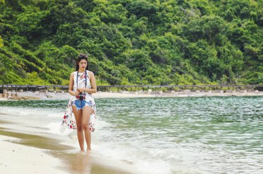 Kadın mutlu gülümseyerek ve sahilde güzel bir fotoğraf makinesi almak. Güzel kız Asya uzak sıradan görünümlü ve gülümseme, gülüyor. Sahilde güzel parlak gökyüzü