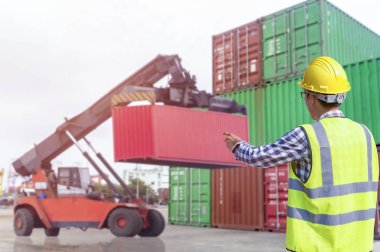 Ustabaşı kontrolü, kargo nakliye gemisinden ithal etmek için konteynır kutusu yüklüyor..