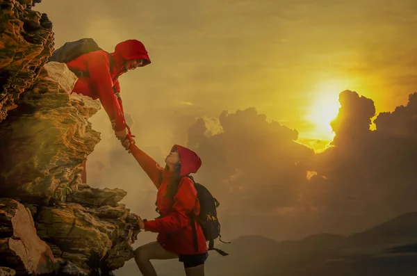 Erkek ve dişi yürüyüşçüler dağ uçurumuna tırmanıyor ve içlerinden biri yardım eli uzatıyor. Yardım eden insanlar ve takım çalışması konsepti.