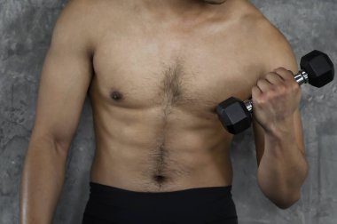 Kaslı vücut geliştirmeci adam çimento zemin üzerine spor salonunda dumbbells ile yapıyor.