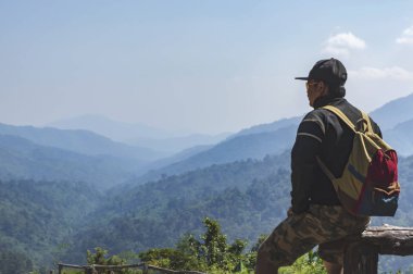 Bir dağın tepesinde oturan sırt çantası ile genç adam uzun yürüyüşe çıkan kimse.
