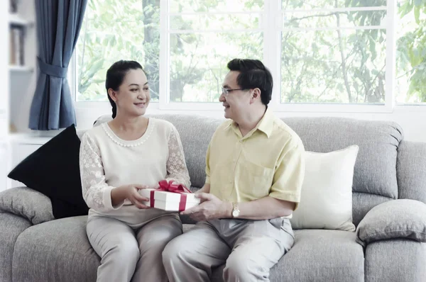 Glückliches Seniorenpaar Tauscht Geschenkschachtel Während Sich Hause Wohnzimmer Entspannt Bild — Stockfoto