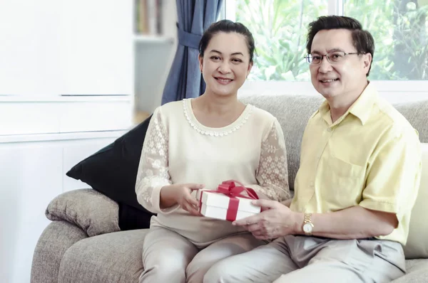 Gelukkige Senior Paar Uitwisselen Van Gift Box Terwijl Ontspant Thuis — Stockfoto