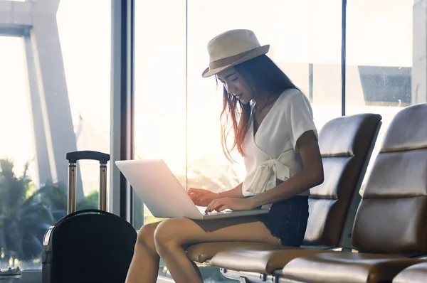 Young woman in airport waiting for air travel using tablet. She is sitting with travel suitcase trolley, in waiting hall of departure lounge in airport.Travel Concept .