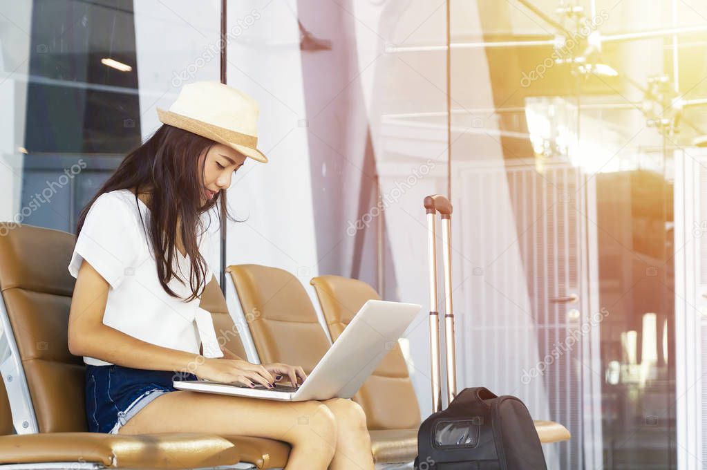 Young woman in airport waiting for air travel using tablet. She is sitting with travel suitcase trolley, in waiting hall of departure lounge in airport.Travel Concept . 