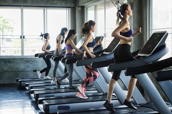 Grup içinde modern spor koşu bandı üzerinde çalışan genç kadın insan
