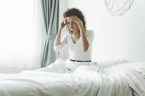 Junge Frau mit Kopfschmerzen, sie sitzt auf dem Bett. — Stockfoto