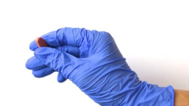 Doktor mavi bir eldiven içinde ilacı çevirir. Kapsül izole bir arka planda. Virüs ve hastalıkların tedavisi.