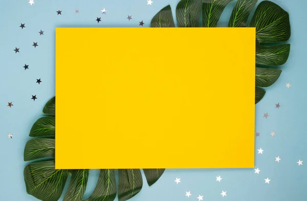 Żółty Arkusz Papieru Kolorowym Konfetti Liściach Tropikalnych Miękkim Niebieskim Tle — Zdjęcie stockowe