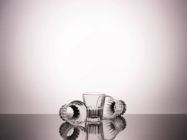 灰色のグラデーションの背景に強いアルコール飲料用の空のガラス ガラス製品の創造的な撮影 — ストック写真