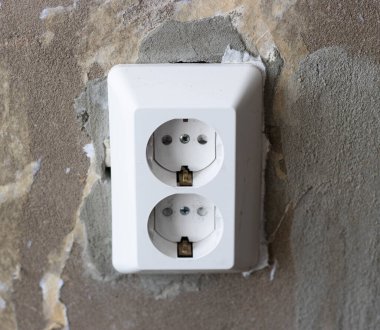 Gri bir duvarda elektrikli beyaz bir soket. Tamir konsepti, elektrik kablolarının değiştirilmesi