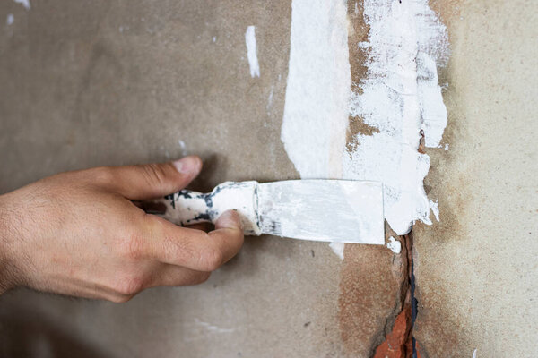 a hand puts putty paste on the wall. sealing of walls. the concept of repair