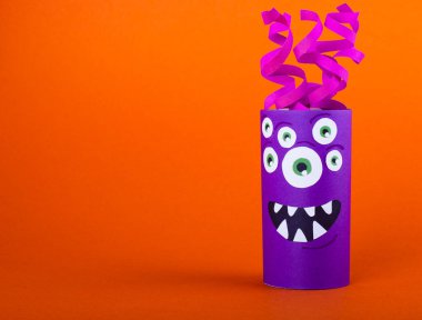 Turuncu arka planda tuvalet kağıdı rulosundan yapılmış korkunç bir canavar. El yapımı sevimli canavarlar.