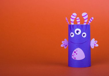 Turuncu arka planda tuvalet kağıdı rulosundan yapılmış mavi korkunç canavar. El yapımı sevimli canavarlar.
