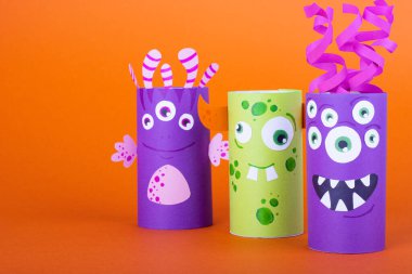 Turuncu arka planda tuvalet kağıdından yapılmış çok renkli canavarlar. El yapımı sevimli canavarlar.