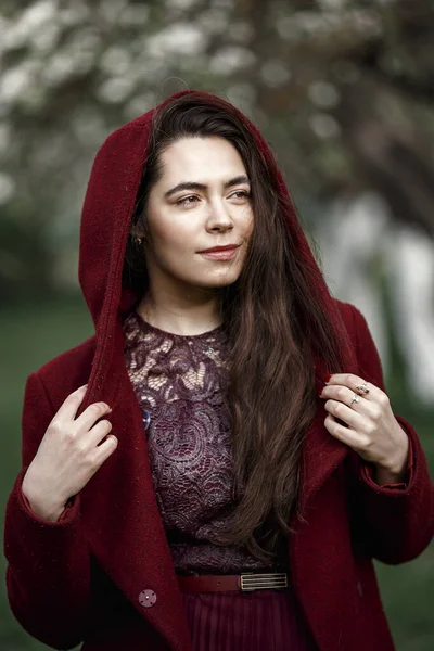 Çiçekli bahçede kestane rengi ceketli bir kız.