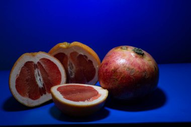 Dilimlenmiş greyfurt ve tüm nar mavi arka planda.