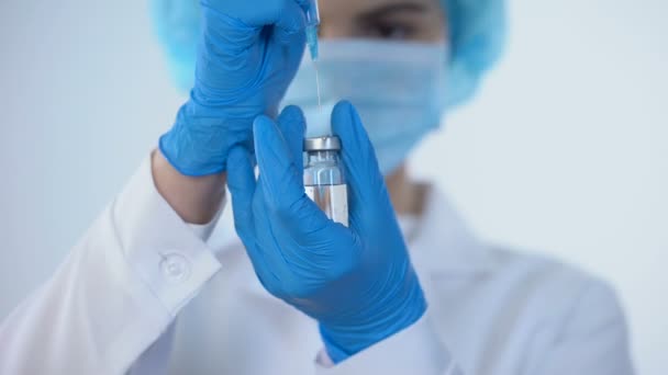 Медсестра на маске, принимающая вакцину со шприцем из ампулы, новые исследования лекарств — стоковое видео
