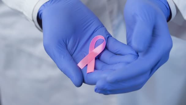Hände in Handschuhen halten vorsichtig ein rosafarbenes Band, Symbol des Brustkrebsbewusstseins — Stockvideo