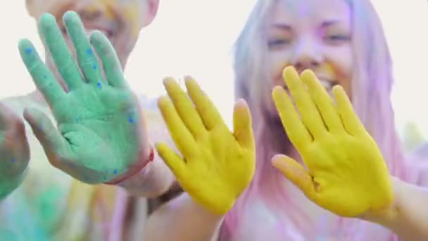 Щасливі друзі махають руками пофарбованими в барвистий порошок, жестикулюючи привіт, вечірка — стокове відео