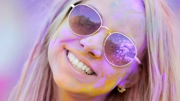 Chica joven en gafas de sol pintadas en polvo de colores sonriendo a la cámara, primer plano — Vídeos de Stock