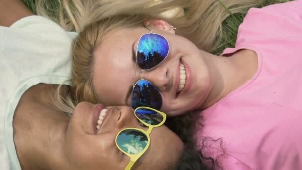 Красивые улыбающиеся девушки в солнечных очках, лежащие на траве, досуг в кампусе — стоковое видео