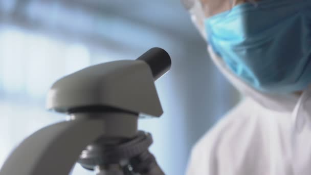 Mężczyzna laborant w maskę ochronną i okulary za pomocą mikroskopu dla badań — Wideo stockowe