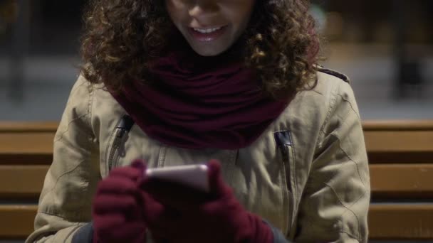 Menina de raça mista alegre atraente usando smartphone com luvas, noite ventosa — Vídeo de Stock
