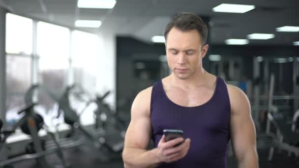 Мужчина проверяет фитнес-приложение в смартфоне, персональную программу онлайн — стоковое видео