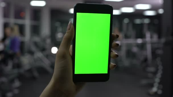 Vrouwelijke hand met smartphone in de sportschool, groen scherm, online fitness toepassing — Stockvideo