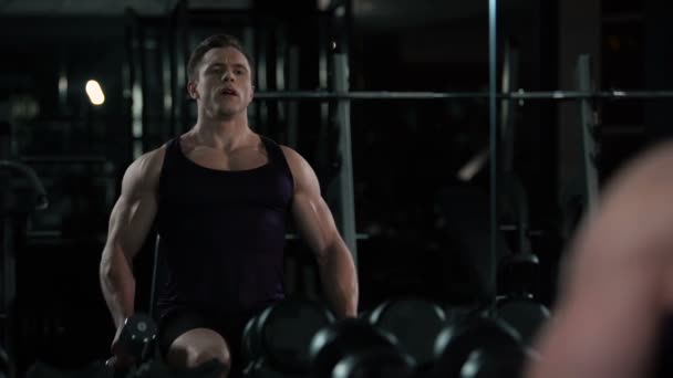 Homem atleta realizando sentado halteres frente levantar, olhando para si mesmo no espelho — Vídeo de Stock