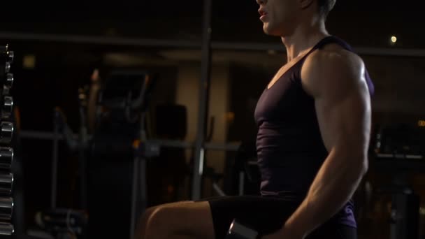 Сексуальный мускулистый мужчина сидит на скамейке и поднимает гантели, спорт — стоковое видео
