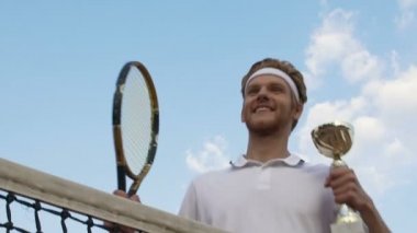 Yakışıklı adam kupa ve raket üzerinde baş gösteren turnuva zaferini kutluyor