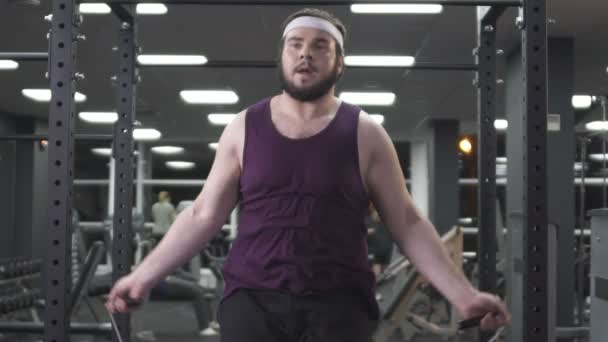 Hombre regordete saltar la cuerda en el gimnasio, calentando antes de agotar el entrenamiento, lento-mo — Vídeos de Stock