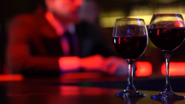 Copas de vino en la mesa del bar sobre fondo de pareja feliz, amantes disfrutando de la fecha — Vídeo de stock