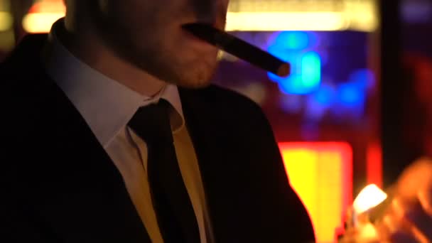 Confident man in suit lighting cigar, relaxing at night party, elite mens club — Stock Video