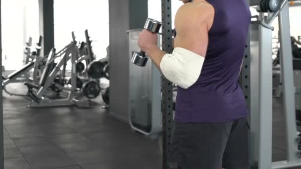 Deportista con el codo lesionado levantando lentamente la mancuerna, recuperación, problema de salud — Vídeos de Stock