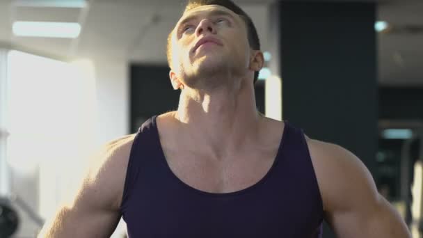Спортсмен прогрівається в ранковому тренажерному залі, сонячне світло падає на м'язове чоловіче тіло — стокове відео