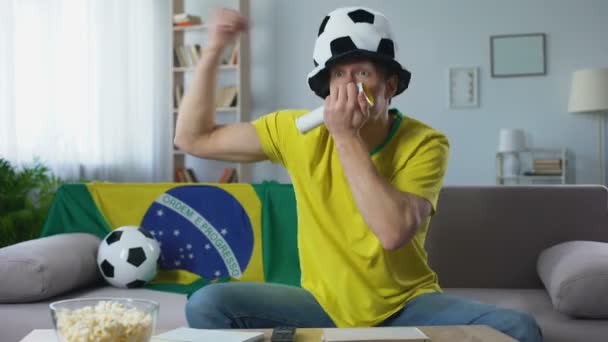 Футбольный болельщик активно поддерживает сборную Бразилии на чемпионате, наблюдая за матчем — стоковое видео