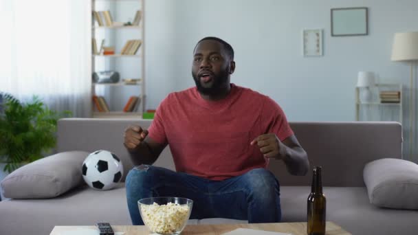 Афро-американец смотрит спортивные соревнования, счастливый фанат победно кричит — стоковое видео