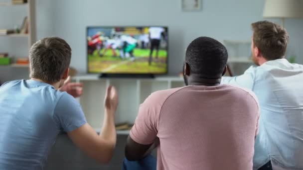 Manliga vänner samlas för att titta på fotboll konkurrens på storbildsskärm, soffa experter — Stockvideo