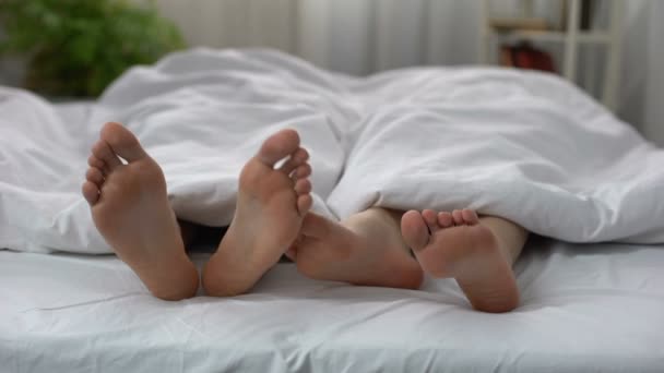 Женские ноги флиртуют с мужчиной в постели, пара имеет интимные проблемы, отношения — стоковое видео
