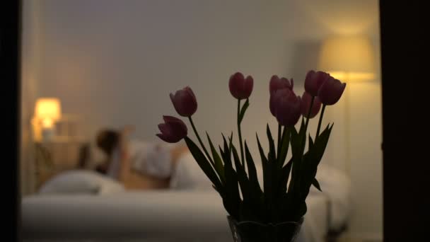 情熱的な恋人のキスと、親密さの背後にあるベッドと素敵なチューリップの花束 — ストック動画