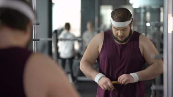 Hombre midiendo la cintura gorda, insatisfecho con su resultado después de la dieta y el entrenamiento — Vídeos de Stock