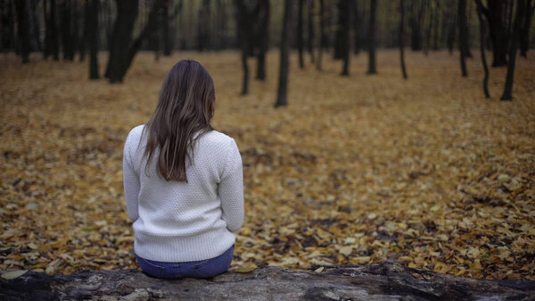 Upset woman sitting in autumn park, melancholy season, depression, loneliness