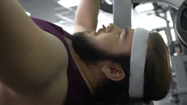 Мотивированный толстяк поднимает штангу спортзала лежа на скамейке, желание похудеть — стоковое видео