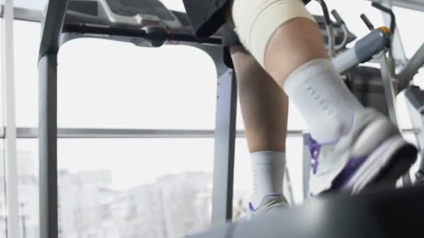 Maschio con muscolo della gamba ferito che cammina sul tapis roulant in palestra, recupero, forza di volontà — Video Stock